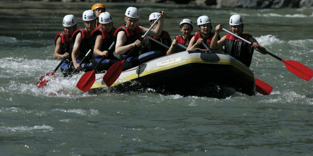 Eine Gruppe von Personen mit Helmen und Schwimmwesten paddelt auf einem Schlauchboot durch einen Fluss mit felsigen Ufern.