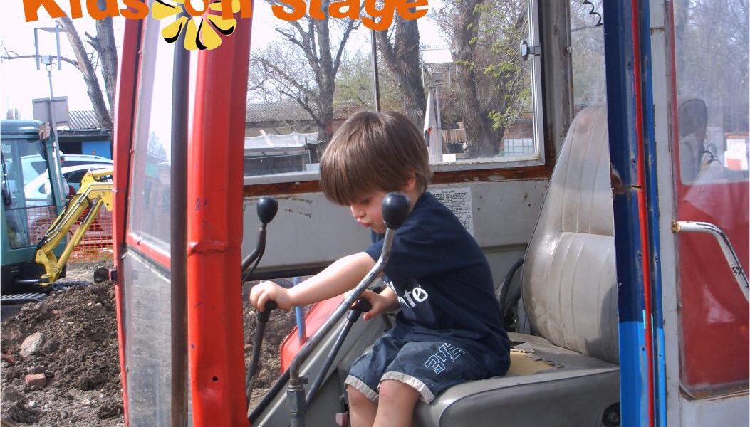 Ein kleines Kind sitzt auf dem Fahrersitz einer Baumaschine und hält die Steuerung in der Hand. Oben ist der Text "Kids on Stage" eingeblendet. In der Ecke erscheint das Datum "2009-04-05".