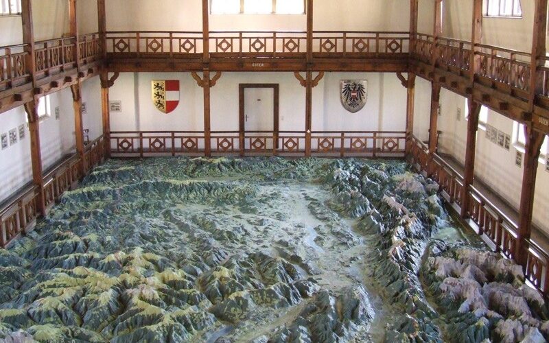 Großes 3D-Geländemodell einer Gebirgslandschaft in einer Holzhalle mit Balkonen und Wappen an den Wänden.