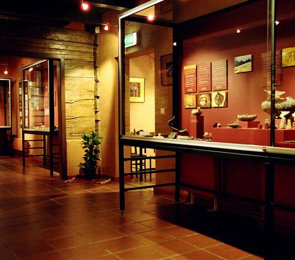 Innenraum des Museums mit Glasvitrinen, in denen Artefakte ausgestellt sind, und Informationstafeln an den Wänden, die mit warmem Licht beleuchtet werden.