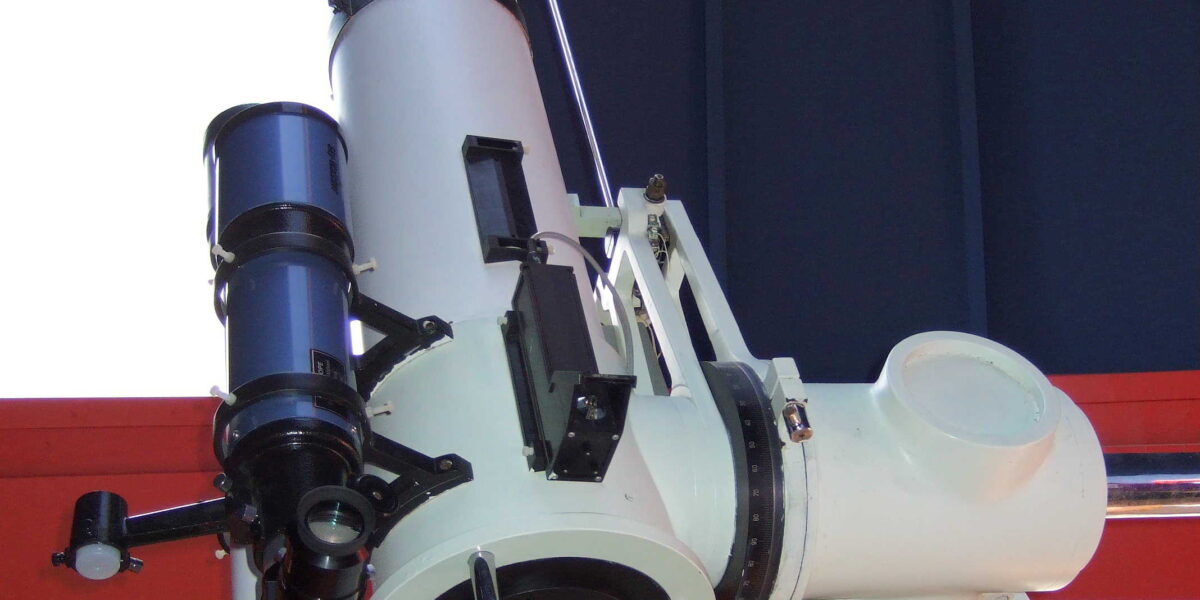 Ein großes weißes Teleskop, das in einer Observatoriumskuppel montiert und auf einen offenen Teil der Kuppel ausgerichtet ist.