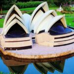 Ein verkleinertes Modell des Opernhauses von Sydney steht neben einem Teich, umgeben von grünem Gras und bunten Blumenbeeten.