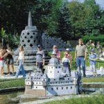 Eine Gruppe von Menschen, darunter Kinder und Erwachsene, steht im Freien und betrachtet Miniaturnachbildungen berühmter Wahrzeichen inmitten von Grünflächen.