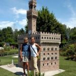 Zwei Mädchen stehen an einem sonnigen Tag vor einem detaillierten Miniaturmodell eines schlossähnlichen Gebäudes im Freien.