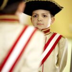 Ein kleiner Junge in einer historischen Militäruniform mit Zweispitz und rot-weißer Schärpe steht vor einem Spiegel.