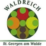 Logo für Waldreich St. Georgen am Walde mit einem kreisförmigen Design mit verschiedenen grünen, roten und orangefarbenen Kreisen und dem Namen ober- und unterhalb der Grafik.
