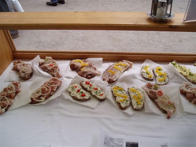 Offene Sandwiches mit verschiedenen Belägen, darunter geschnittene Zwiebeln, cremige Aufstriche, Kräuter und geschnittene Paprika, die auf weißen Servietten auf einer Holztheke angerichtet sind.
