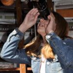 Eine Person in einer Jeansjacke schaut im Innenbereich durch das Okular eines großen Teleskops.