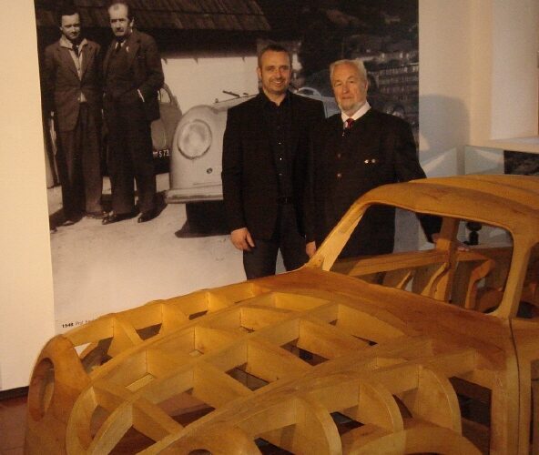 Zwei Männer stehen vor einem großen alten Foto und neben einem hölzernen Autorahmen, der in einem Museum ausgestellt ist.