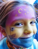 Kind mit bunter Gesichtsbemalung, die einen Nachthimmel auf der Stirn und ein Piratenschiff auf der Wange zeigt, lächelt in die Kamera.