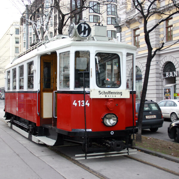 Rot-weiße Oldtimer-Straßenbahn mit der Nummer 4134 hält an einer Straßenbahnhaltestelle in einer von Autos und historischen Gebäuden gesäumten Straße.