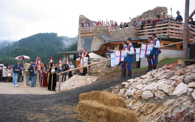 Menschen in mittelalterlichen Kostümen führen in einer steinernen Festung ein Reenactment auf, das von Holzplattformen und vom Boden aus beobachtet wird.