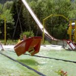 Eine Person fährt mit einem kleinen Boot eine Wasserrutsche hinunter, wobei das Boot knapp über dem Wasser in einem Vergnügungspark in der Luft schwebt.