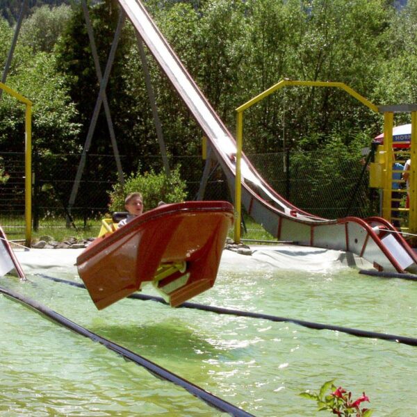 Eine Person fährt mit einem kleinen Boot eine Wasserrutsche hinunter, wobei das Boot knapp über dem Wasser in einem Vergnügungspark in der Luft schwebt.