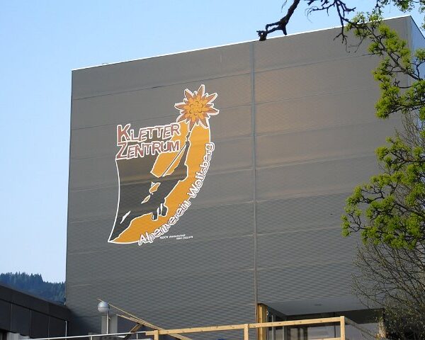 Ein graues Gebäude mit einem großen Schild mit der Aufschrift "Kletterzentrum" und der Abbildung eines Kletterers, eines Berges und einer Edelweißblume.