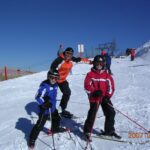 Drei Personen in Skiausrüstung posieren auf einer verschneiten Piste mit Skistöcken, während andere im Hintergrund zu sehen sind; das Datum lautet 2007-02-18.