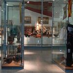 In den Glasvitrinen einer Museumsausstellung sind Marineuniformen, Hüte und Schiffsmodelle ausgestellt, während im Hintergrund verschiedene maritime Artefakte zu sehen sind.