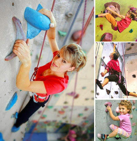 Eine Frau und drei Kinder klettern mit bunten Griffen an Indoor-Felswänden, die jeweils mit Gurten und Seilen gesichert sind.