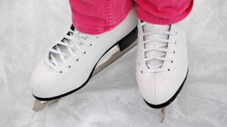 Eine Person in weißen Schlittschuhen und rosa Hosen steht auf einer Eisbahn.