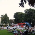 Man kann sich auf Liegestühlen entspannen und in einem öffentlichen Freibad mit roter Rutsche, Wasserspielen und umliegenden Bäumen schwimmen.