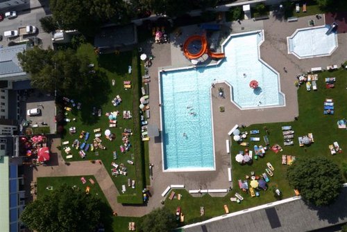 Luftaufnahme eines öffentlichen Schwimmbads mit schwimmenden und sich sonnenden Menschen auf Liegestühlen auf der Wiese.