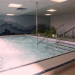 Ein überdachter Whirlpool mit sprudelndem Wasser, Handläufen, gefliesten Wänden und Topfpflanzen am Rande.