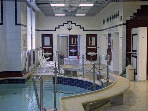 Innen-Spa-Bereich mit einem kleinen runden Pool, weißen Liegestühlen, gefliesten Wänden, Spiegeln und Waschbecken an der Rückwand.