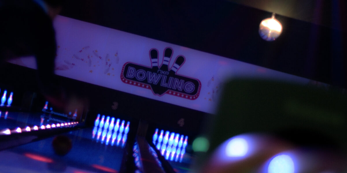 Eine leuchtende Bowlingbahn mit Neonlicht und einem Schild mit der Aufschrift "Bowling" über den Bahnen; am Ende der Bahnen sind Bowlingpins beleuchtet.