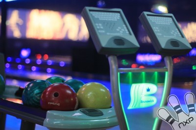 Nahaufnahme einer Bowlingkugel-Rückgabe mit bunten Kugeln und zwei elektronischen Scoring-Bildschirmen in einer Bowlingbahn.