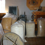 Säcke mit Getreide und Mehl liegen auf einem Holzboden neben den Mühlen in einer rustikalen Halle.