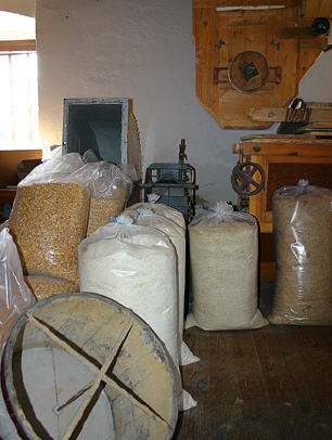 Säcke mit Getreide und Mehl liegen auf einem Holzboden neben den Mühlen in einer rustikalen Halle.