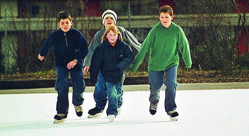 Vier Kinder in Winterjacken und Pullovern, die tagsüber im Freien Schlittschuh laufen.