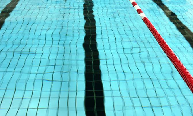Schwimmbadwasser mit Bahnmarkierungen auf dem Boden und einem rot-weißen Bahntrenner, der auf der rechten Seite schwimmt.