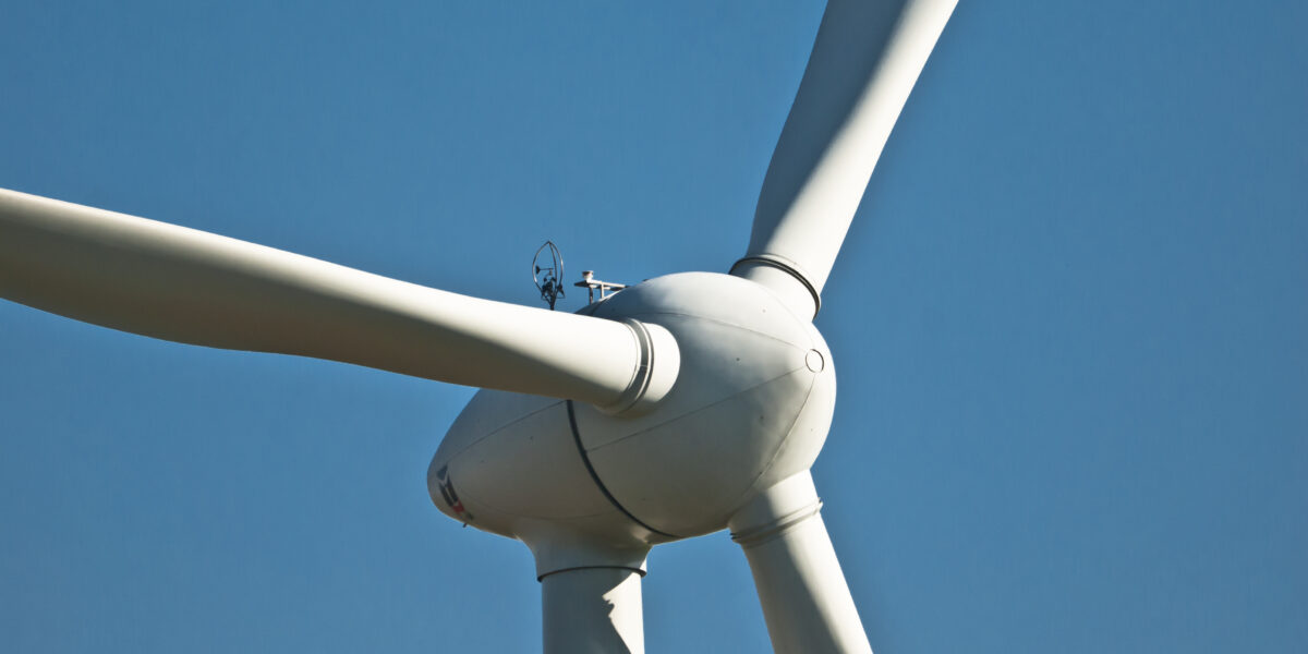 Nahaufnahme einer weißen Windturbine vor strahlend blauem Himmel.