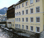 Ein gelbes Gebäude mit der Aufschrift "Kranken-Gebäu" und "Sanatorium Montafon" steht neben einem felsigen Fluss, im Hintergrund sind Berge zu sehen.