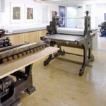 Ein Atelier für Druckgrafik mit großen alten Druckmaschinen und gerahmten Kunstwerken an den Wänden.