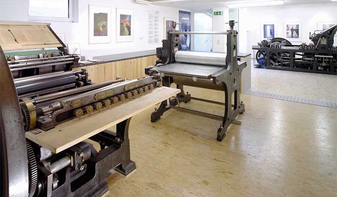 Ein Atelier für Druckgrafik mit großen alten Druckmaschinen und gerahmten Kunstwerken an den Wänden.