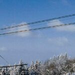 Die Seilbahn mit der Aufschrift "Pfänder" fährt über verschneite Bäume und Landschaften unter einem klaren blauen Himmel; die Einstiegsstation ist links zu sehen.