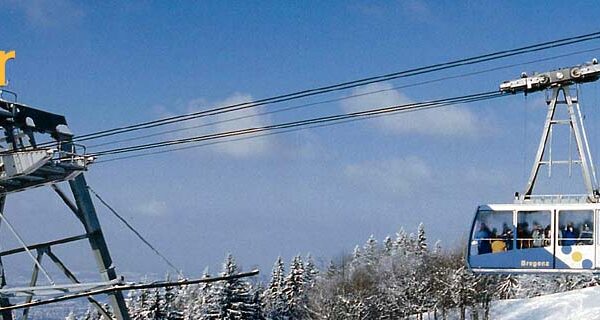 Die Seilbahn mit der Aufschrift "Pfänder" fährt über verschneite Bäume und Landschaften unter einem klaren blauen Himmel; die Einstiegsstation ist links zu sehen.