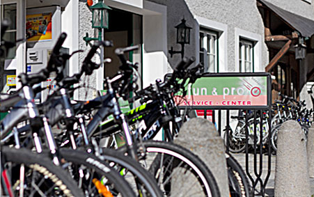 Eine Reihe von Fahrrädern, die vor einem Gebäude mit einem Schild mit der Aufschrift "fun & pro SERVICE CENTER" abgestellt sind.