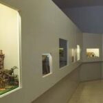 Ein Flur mit mehreren in die Wand eingebauten Schaufenstern, in denen jeweils unterschiedliche Miniaturdioramen oder Szenen gezeigt werden.