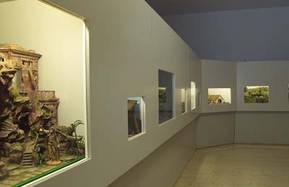 Ein Flur mit mehreren in die Wand eingebauten Schaufenstern, in denen jeweils unterschiedliche Miniaturdioramen oder Szenen gezeigt werden.