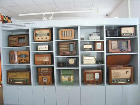 Eine Ausstellung von alten Radios verschiedener Größen und Stile, die in einem Museum oder einer Ausstellung in Regalen angeordnet sind.
