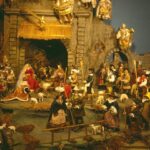 Eine detaillierte Krippe mit Figuren, Tieren und Engeln vor einem Hintergrund aus Stein, die die Geburt Jesu darstellt.