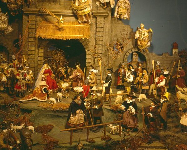 Eine detaillierte Krippe mit Figuren, Tieren und Engeln vor einem Hintergrund aus Stein, die die Geburt Jesu darstellt.