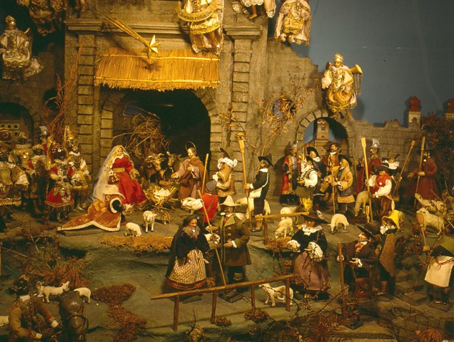 Eine detaillierte Krippe mit Figuren, Tieren und Engeln vor einem Hintergrund aus Stein, die die Geburt Jesu darstellt.