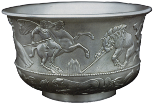 Silberne Schale mit geprägten Figuren, die eine reitende Person auf der Jagd nach einem Löwen darstellen, mit zusätzlichen Tiermotiven im unteren Teil des Gefäßes.