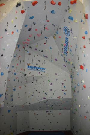 Indoor-Kletterwand mit verschiedenfarbigen Griffen und Tritten, die an weißen Platten befestigt sind, mit leichten Überhängen und Branding an der Wand.