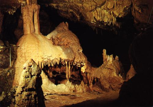 Stalaktiten und Stalagmiten in einer schwach beleuchteten Höhle mit mineralischen Formationen auf dem Boden und an der Decke.