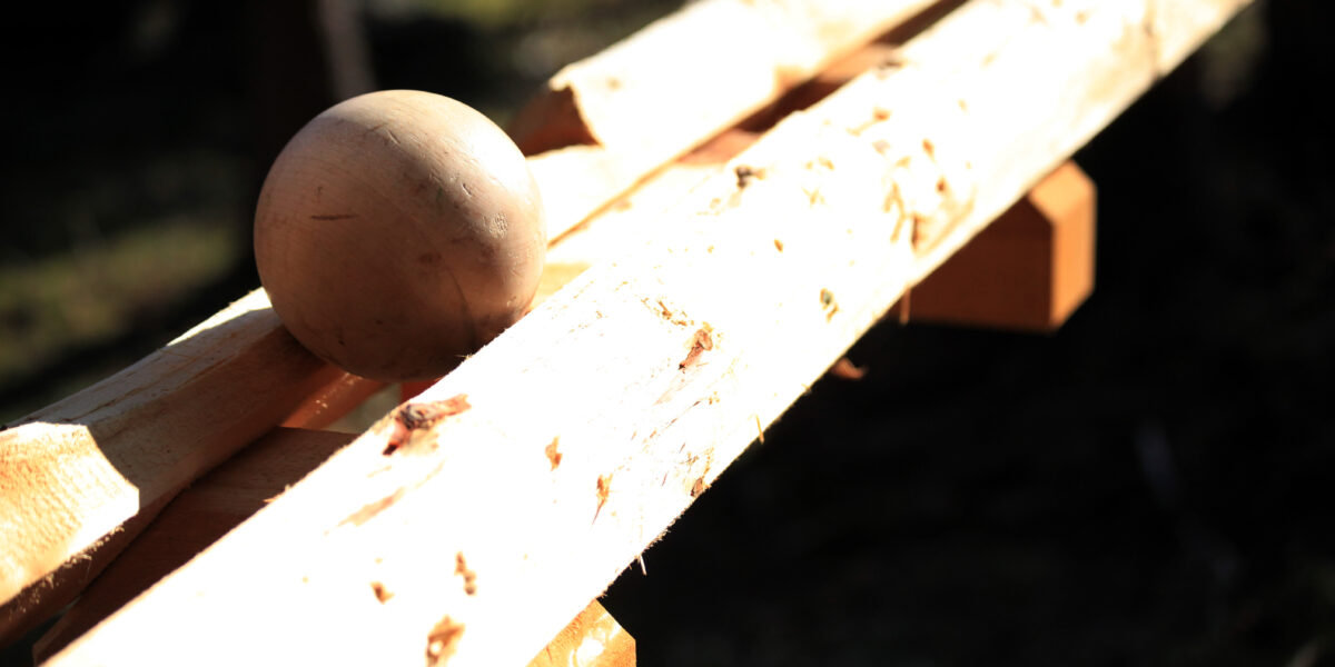 Eine Holzkugel wird auf zwei rauen, unbearbeiteten Holzbrettern im Freien in hellem Sonnenlicht platziert.
